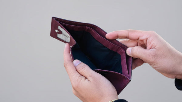 Person holding an empty maroon wallet outdoors with trees in the background