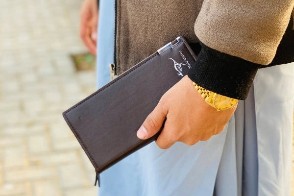 Person holding a black wallet with a blurred outdoor background