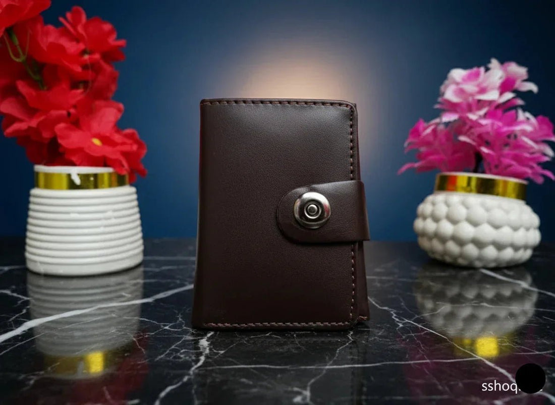 Brown leather wallet with a metallic clasp on a dark marble surface with two vases of flowers.