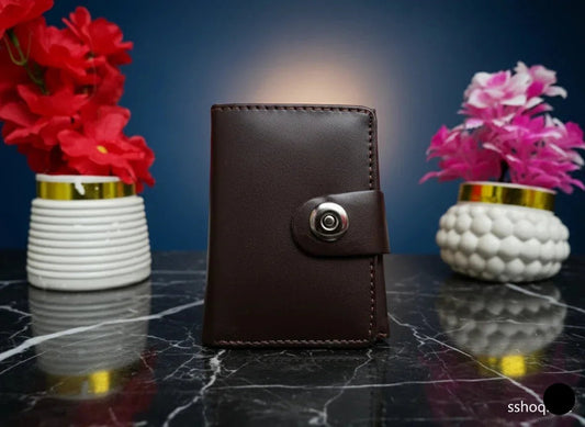 Brown leather wallet with a metallic clasp on a dark marble surface with two vases of flowers.