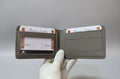 Gray leather wallet held open by a white-gloved hand against a gray background