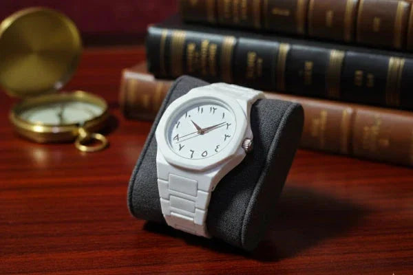 White watch on a black stand with vintage books and pocket watch in the background