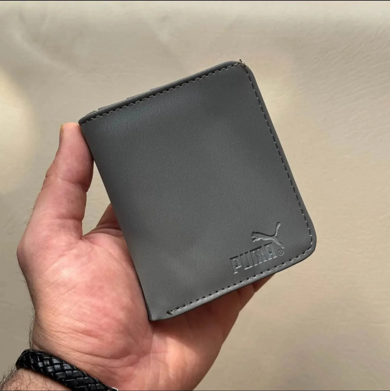 Gray Puma wallet held in a hand against a beige background
