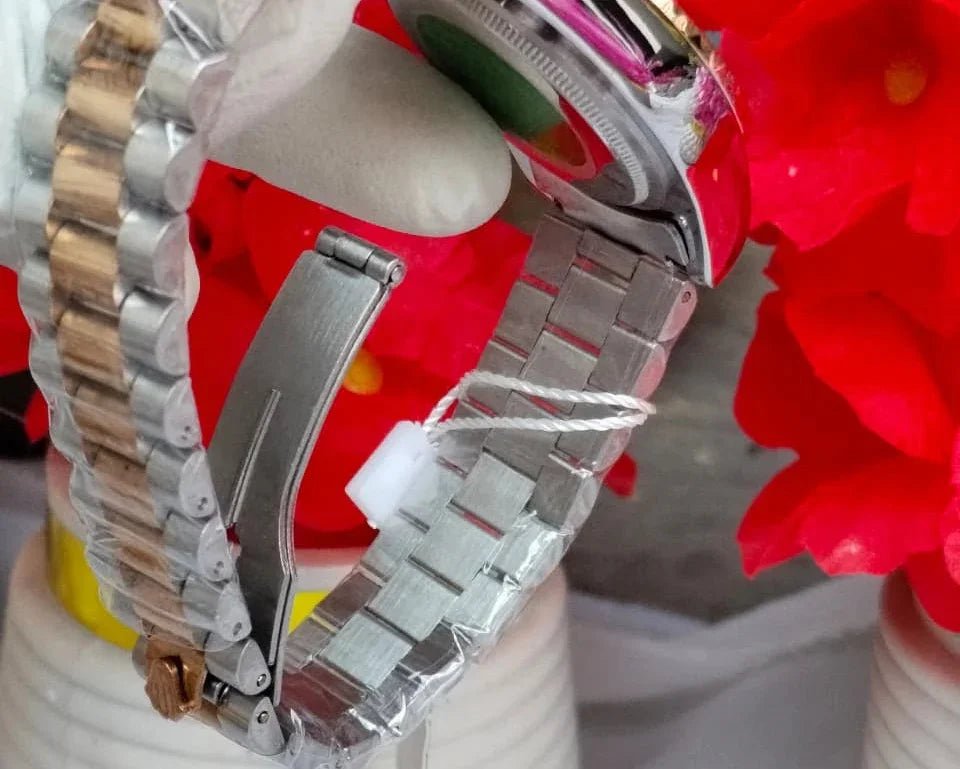 Silver watch with a detailed band on a white stand with a red flower in the background