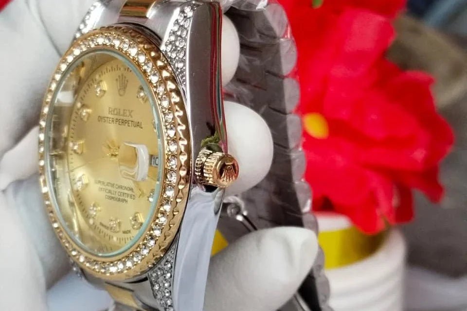 Gold and silver watch with gemstone accents held by a gloved hand against a blurred floral background.
