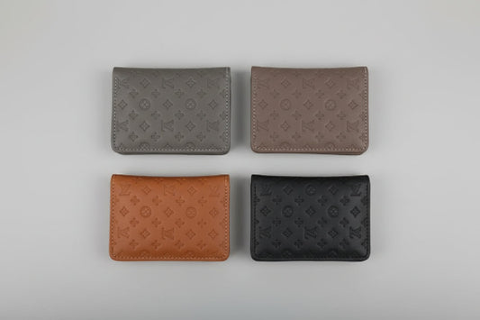 Four different colored wallets with a monogram pattern on a marble surface