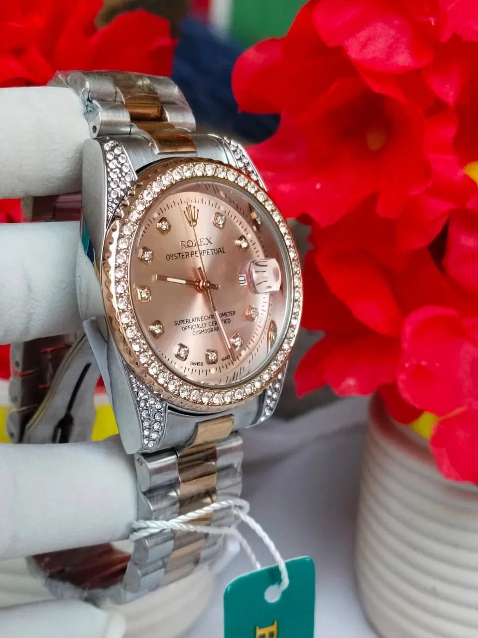 Silver and rose gold watch with gemstones on a white stand with red flowers in the background