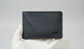 Black wallet held by a gloved hand on a light gray background
