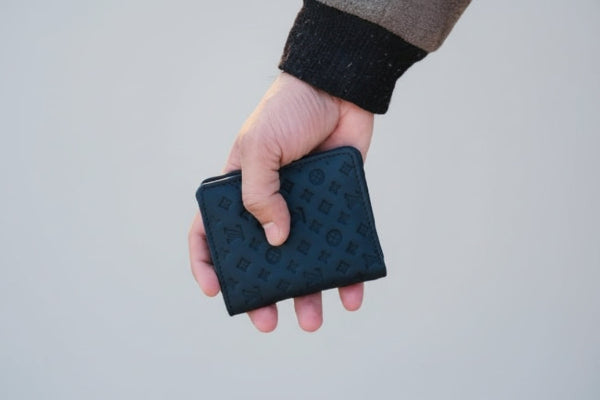 Hand holding a black textured wallet outdoors with a blurred background