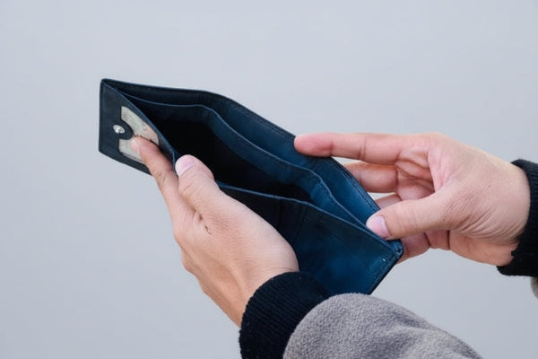 Person holding an empty black wallet outdoors with greenery in the background