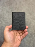 Black textured wallet held in a hand against a gray background