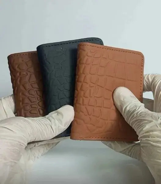 Three leather wallets in brown, black, and brown with a textured pattern held by gloved hands against a light gray background.