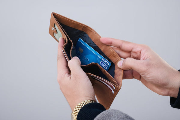 Person holding a brown leather wallet with a blue card inside on a light gray background