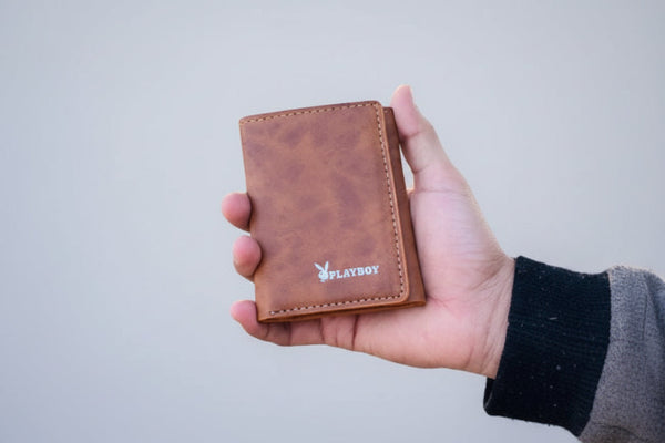 Brown leather wallet with Playboy logo held in a hand outdoors