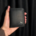 Black Puma wallet held in a hand against a black background