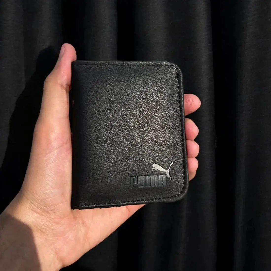 Black Puma wallet held in a hand against a black background