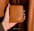 Hand holding a light brown Puma wallet against an orange curtain background